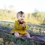 Cute baby girl sitting on a blanket in a park during fall, smiling happily.